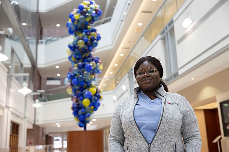 Opibea Aidoo in a scrubs and an Indiana University jacket smiling next to a blue and yellow sculpture.